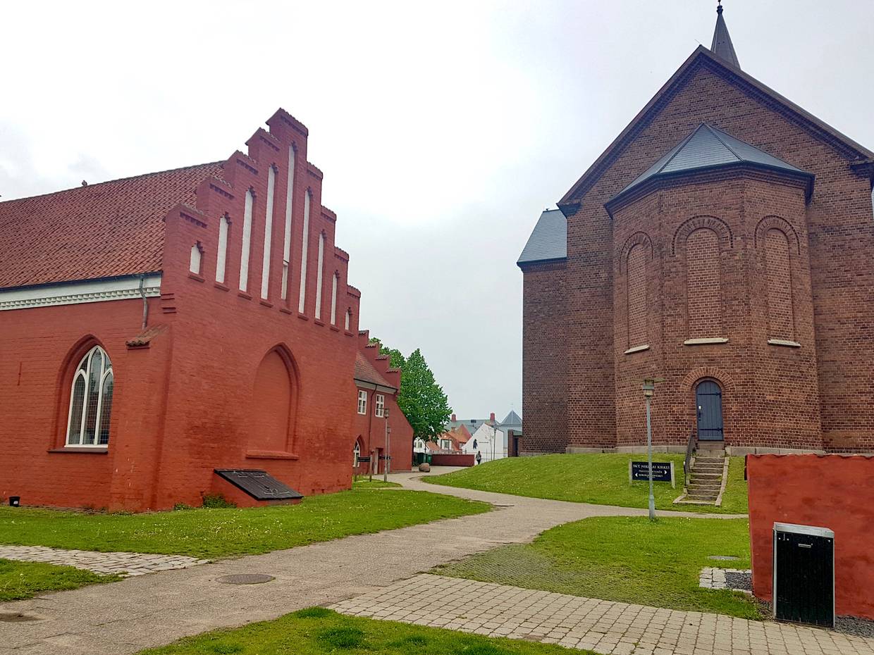 Backsteinkirche neben einem rotgestrichenen Haus, einem ehemaligen Klostergebäude