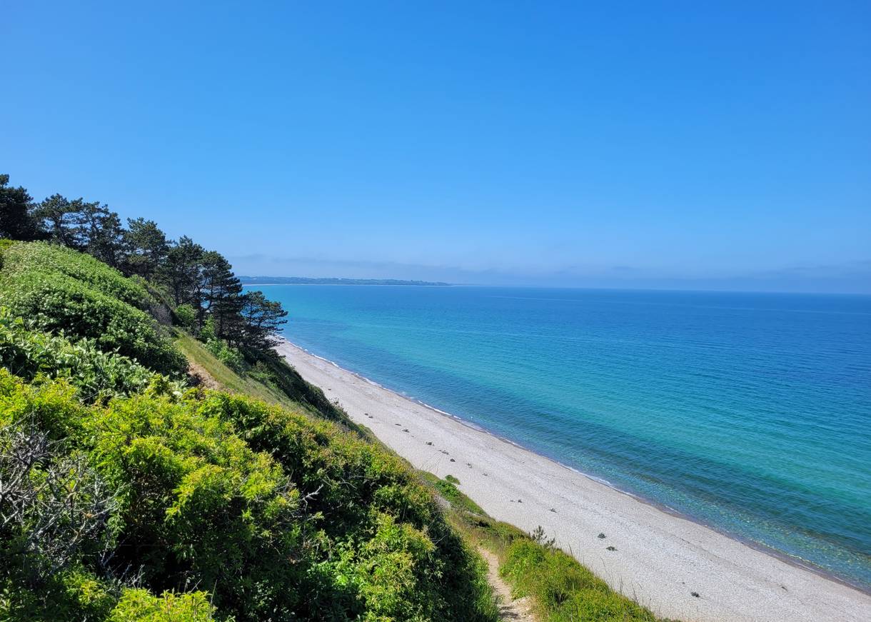 Blick auf blaues Meer und weißen Strand unterhalb einer grünen Steilküste