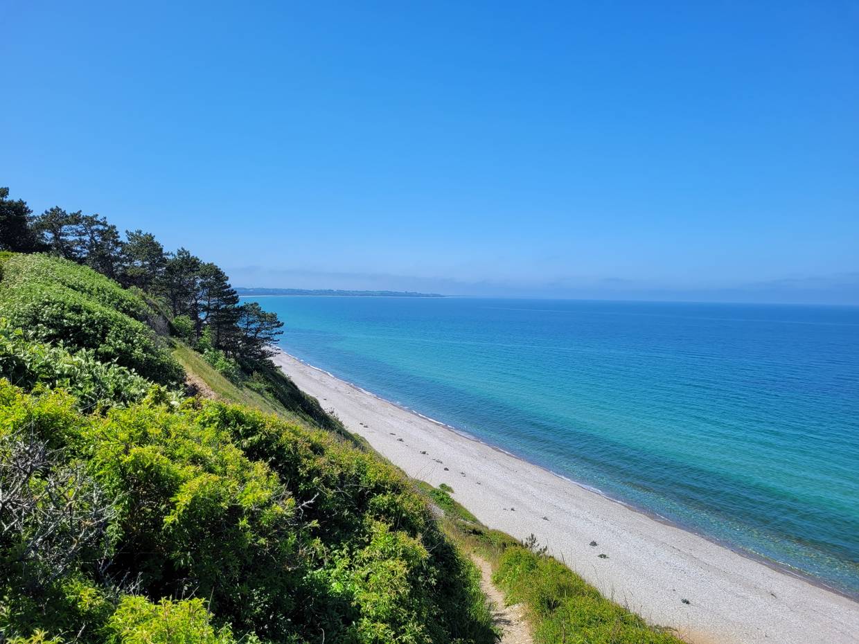 Blick auf blaues Meer und weißen Strand unterhalb einer grünen Steilküste