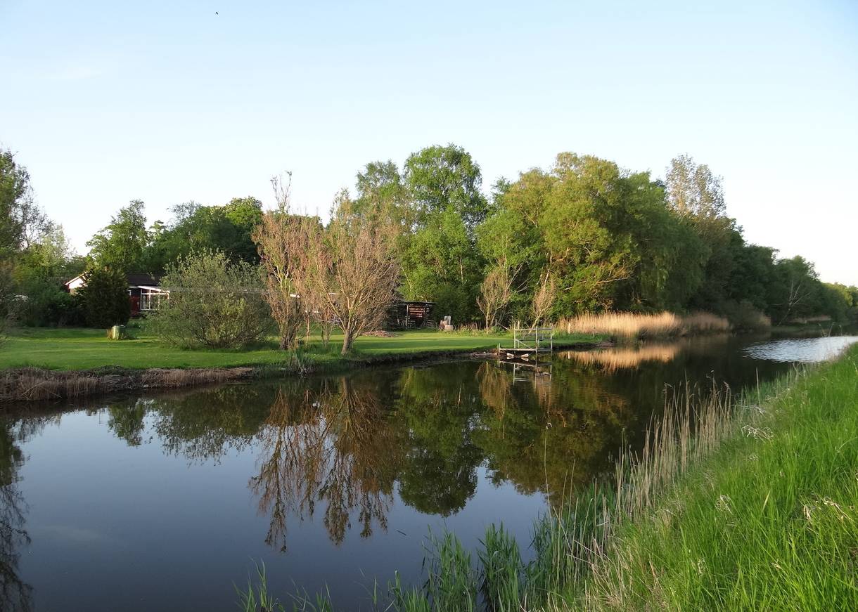 Spigelglatter Kanal zwischen maigrünen Bäumen und Wiesen