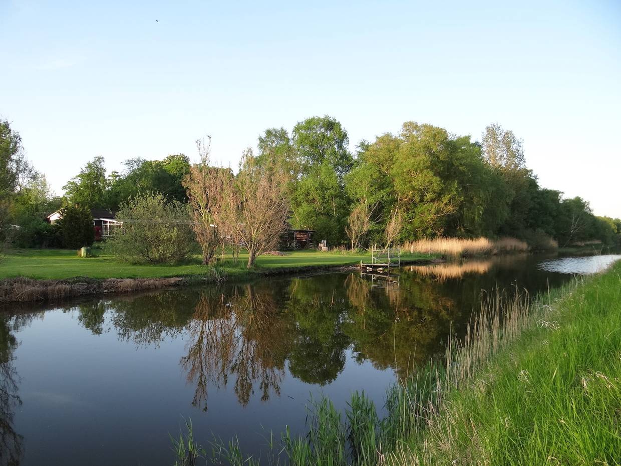 Spigelglatter Kanal zwischen maigrünen Bäumen und Wiesen