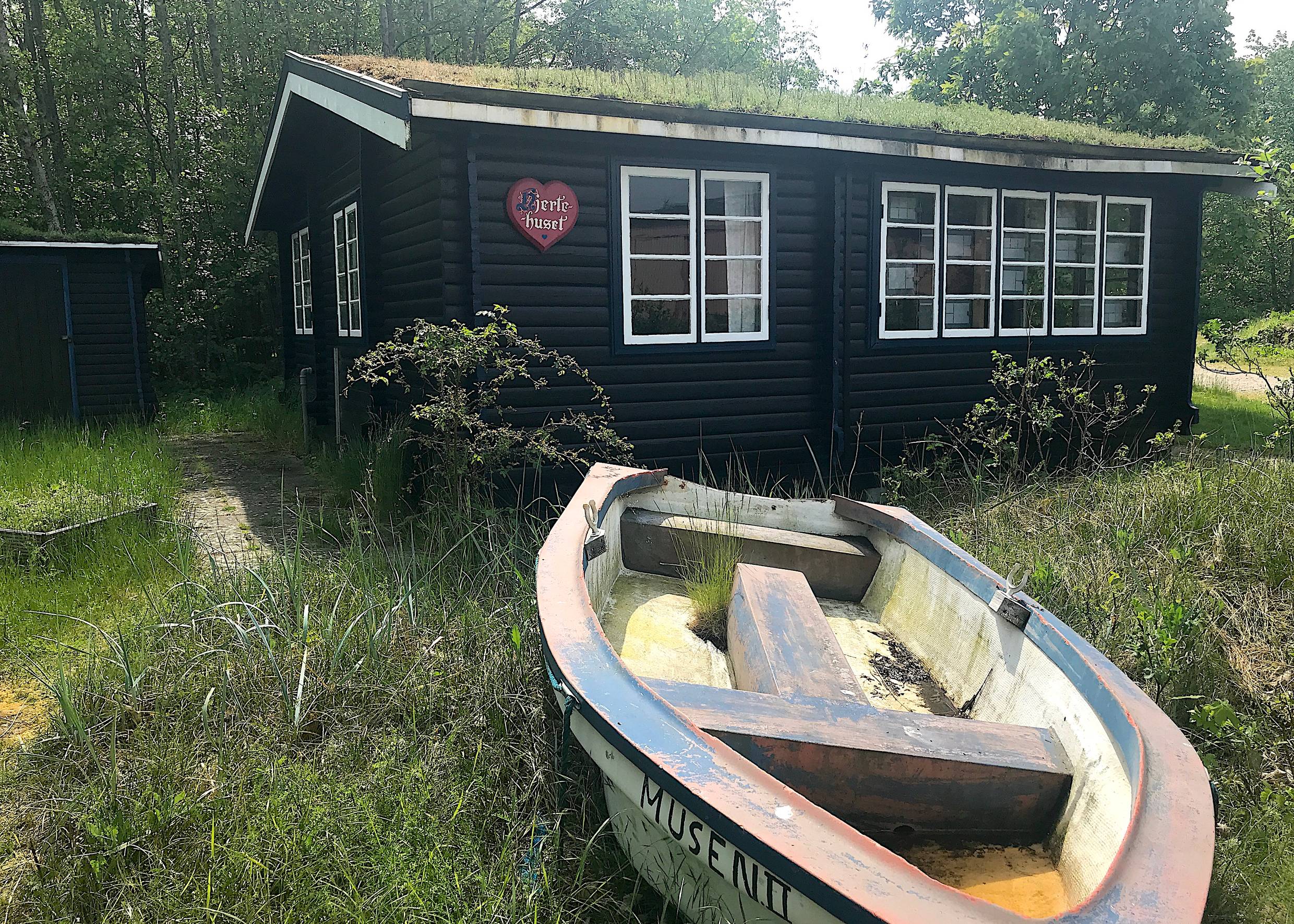 Schwarzes Holzferienhaus, davor ein altes Ruderboot