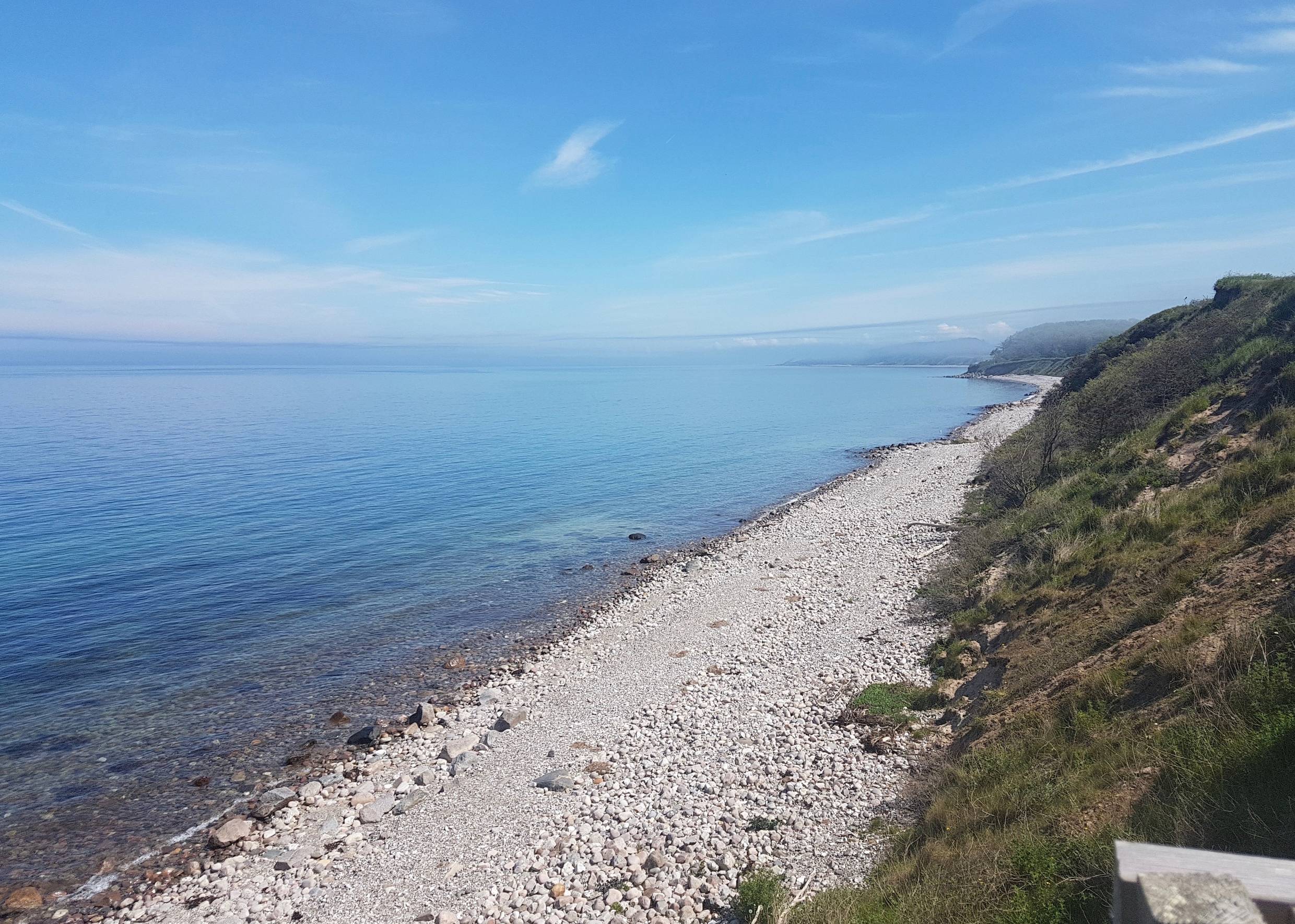 Blick über die steinige Küste mit grünen Hügeln am Ufer