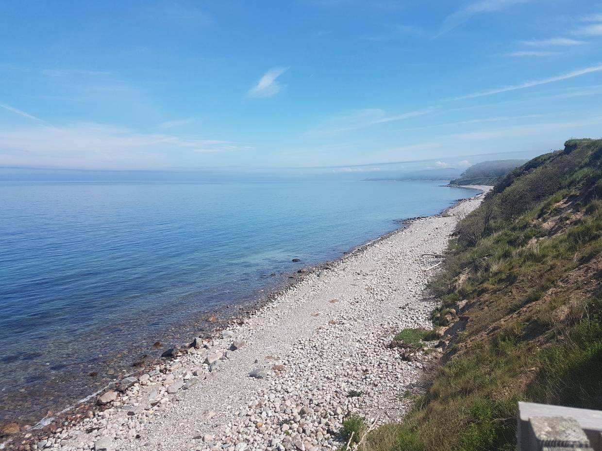 Blick über die steinige Küste mit grünen Hügeln am Ufer