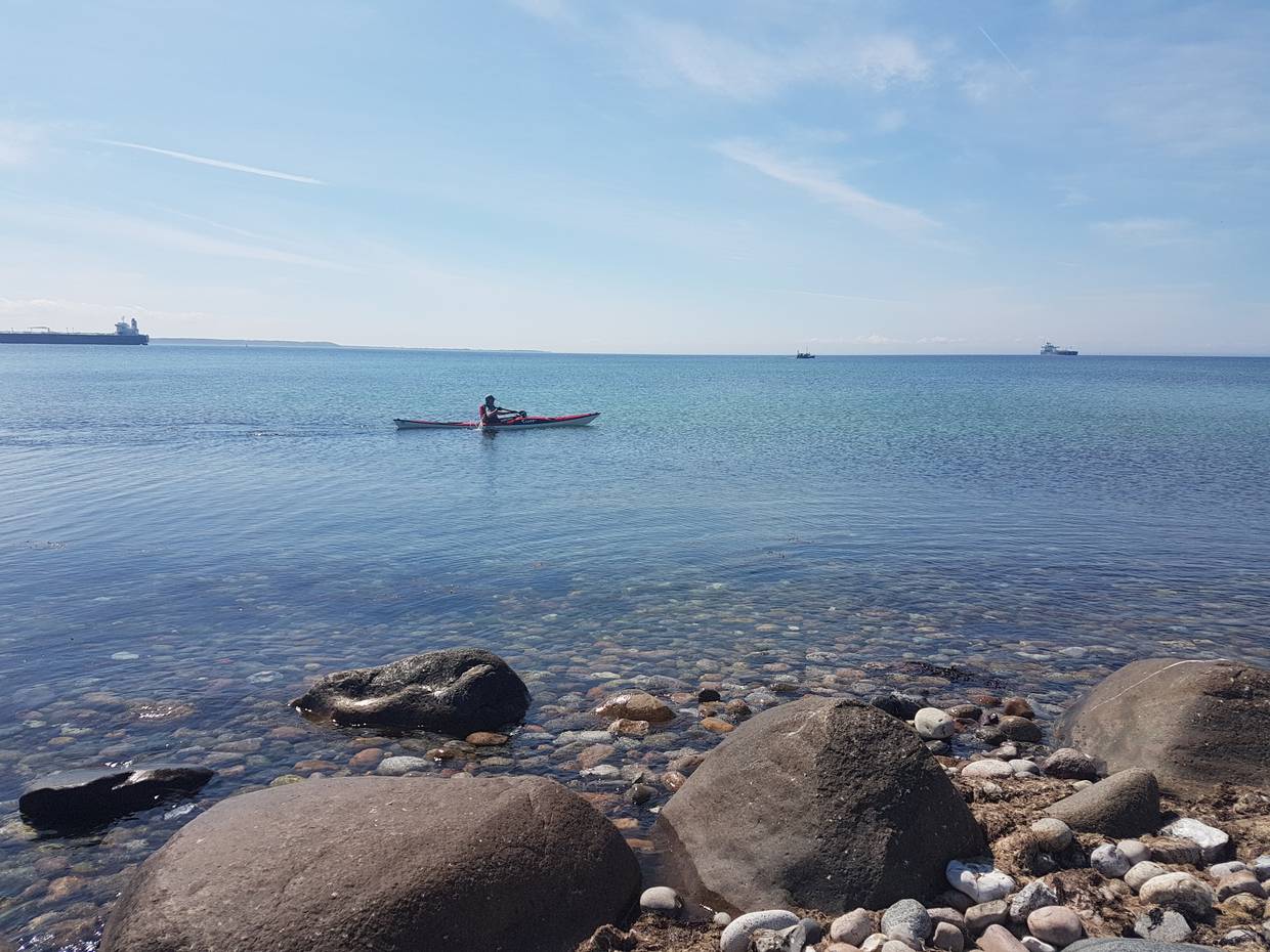 Kajakfahrer auf windstillem Meer, dahinter große Schiffe am Horizont