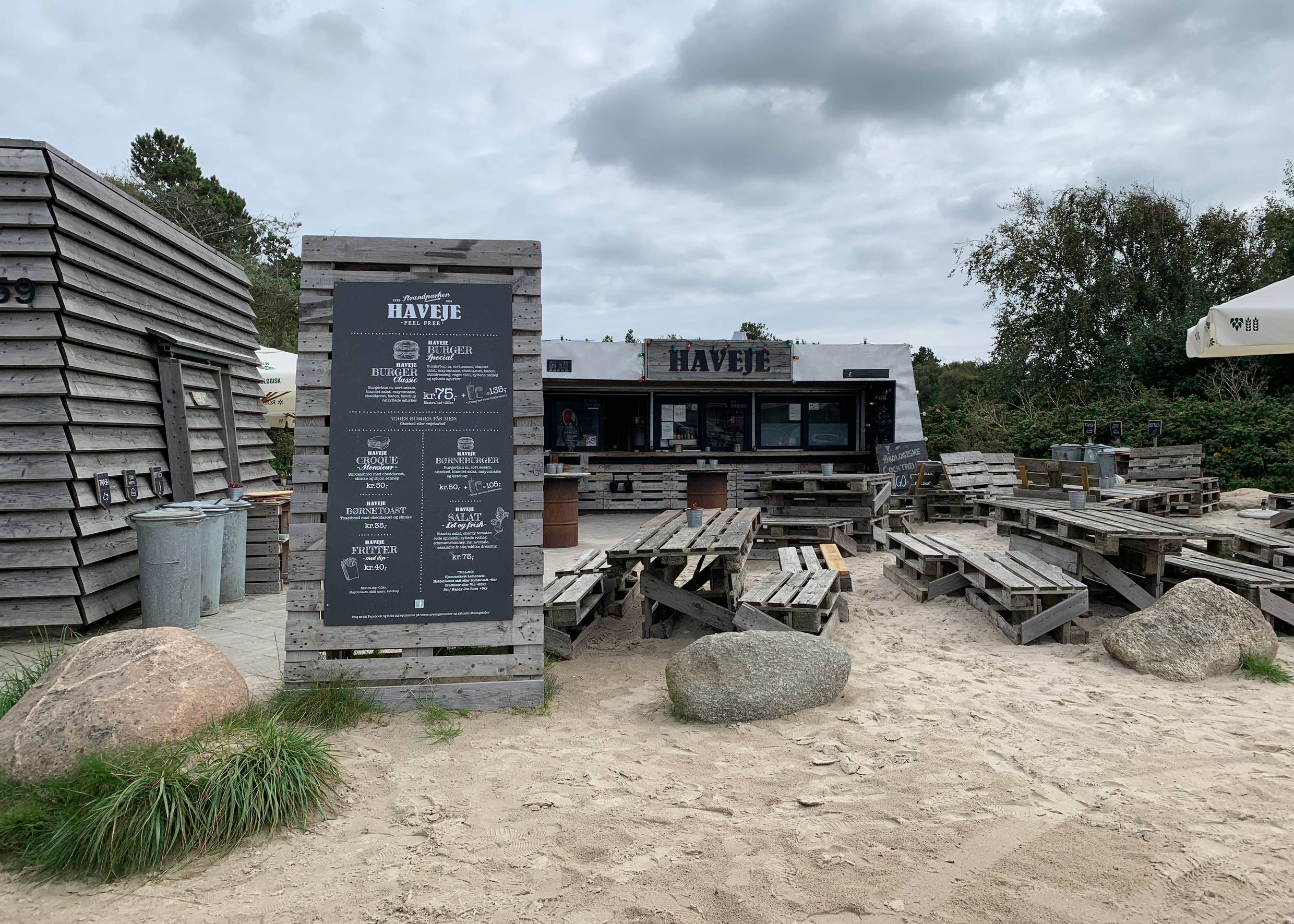 Blick über einen Strandparkplatz, am Ende eine hölzerne Bar