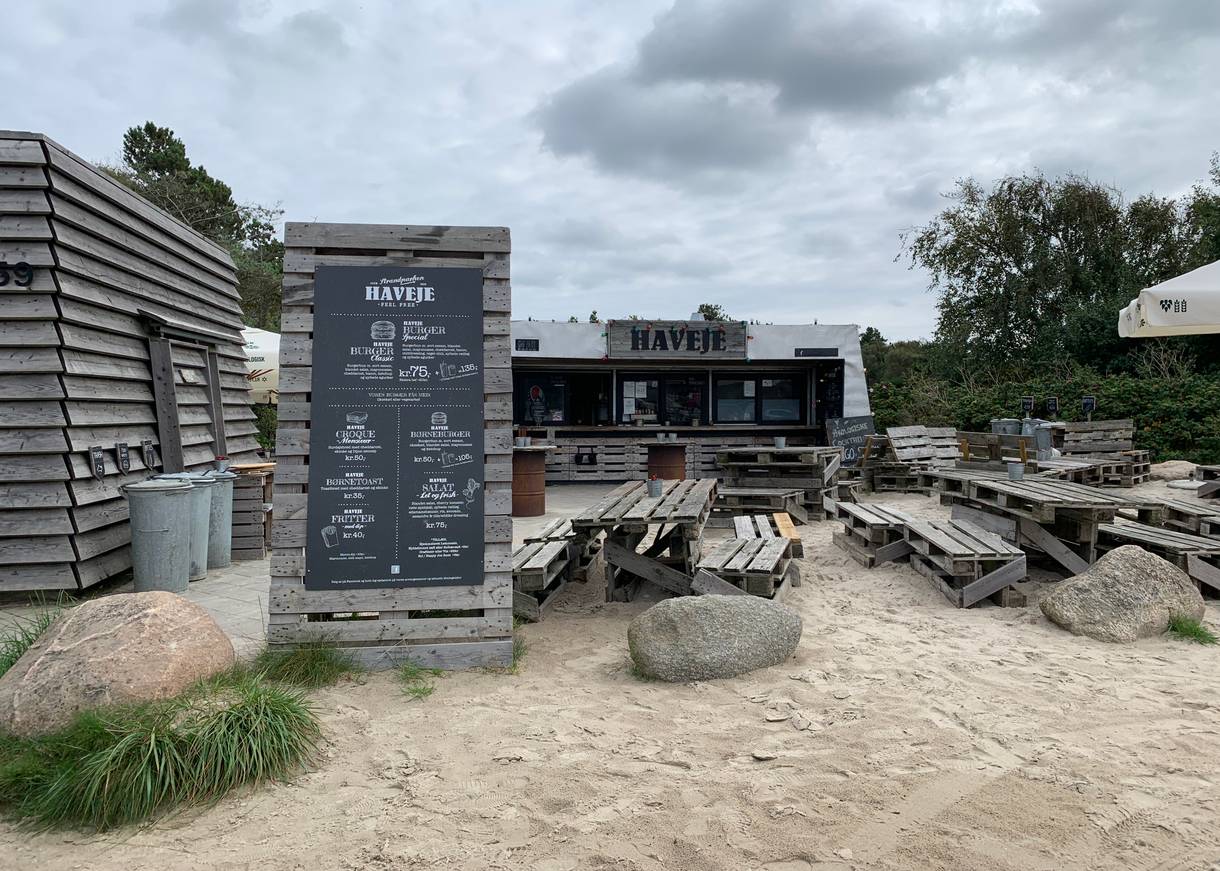 Blick über einen Strandparkplatz, am Ende eine hölzerne Bar
