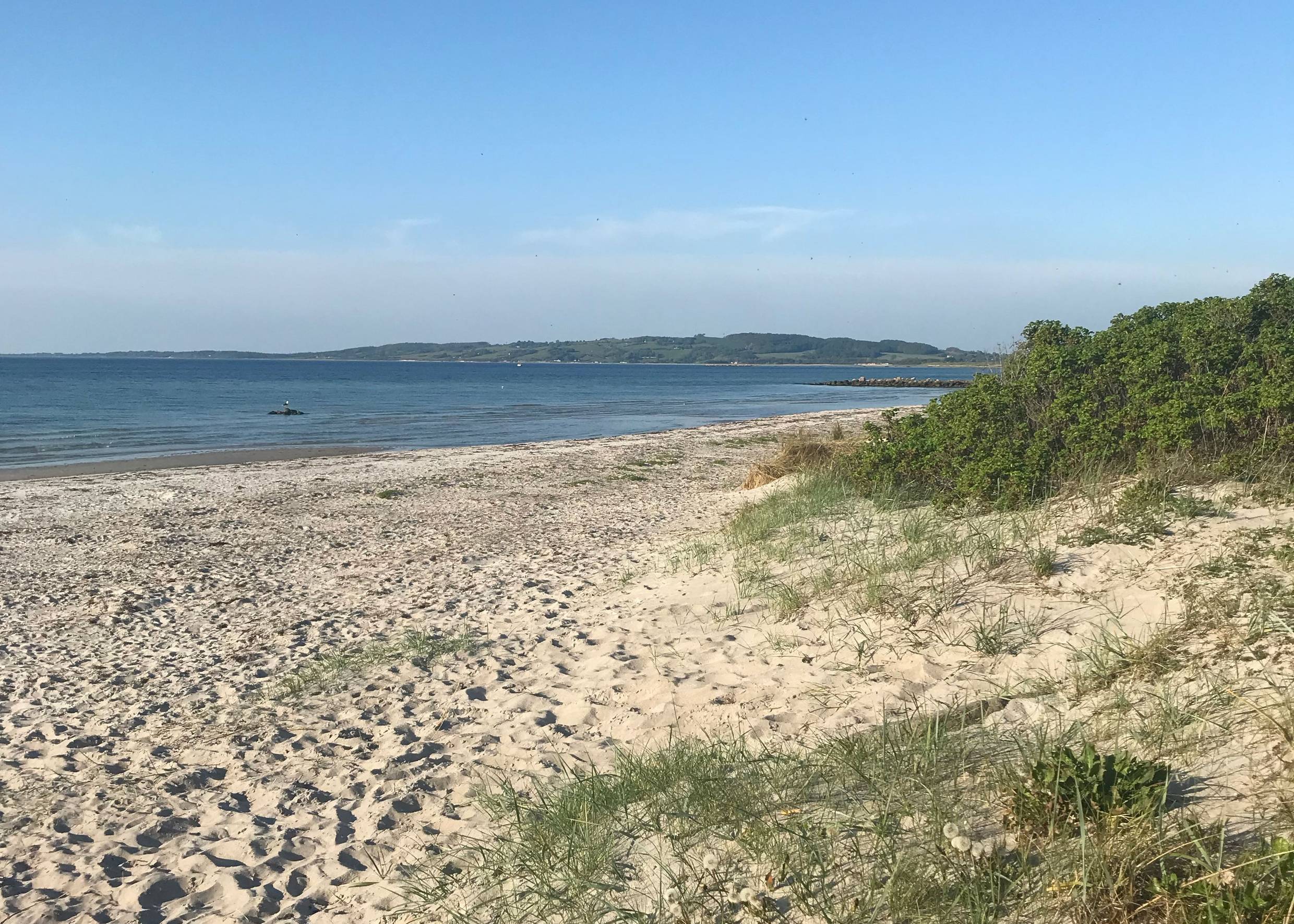 Blick über den Strand, hinter dem Meer ein grüne Anhöhe