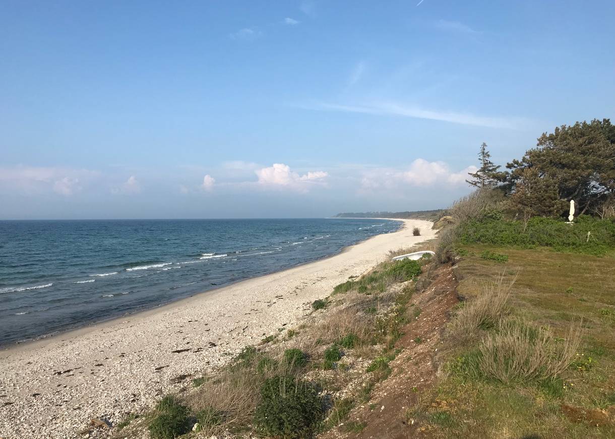 Kiesstrand vor einer grün bewachsenen Steilküste