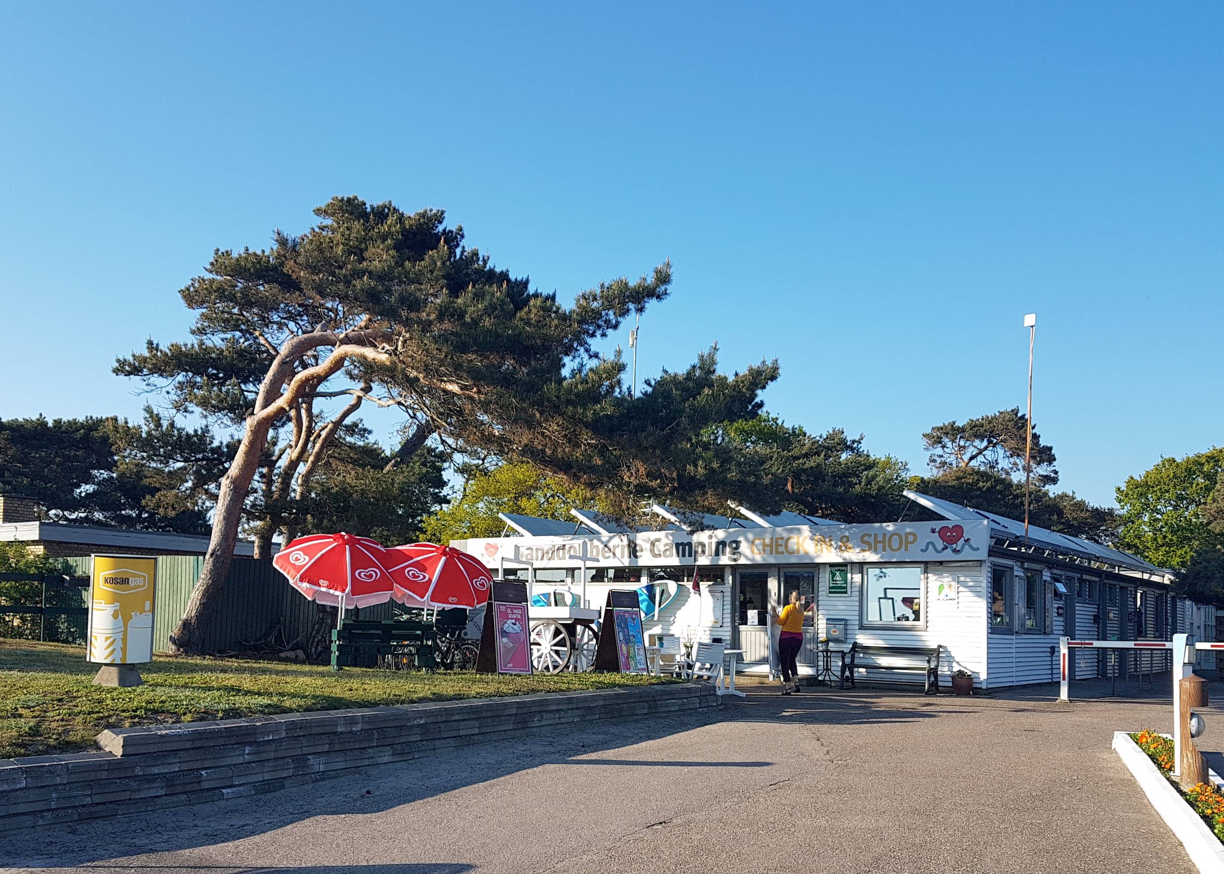 Kiosk am Campingplatz, davor rote Sonnenschirme