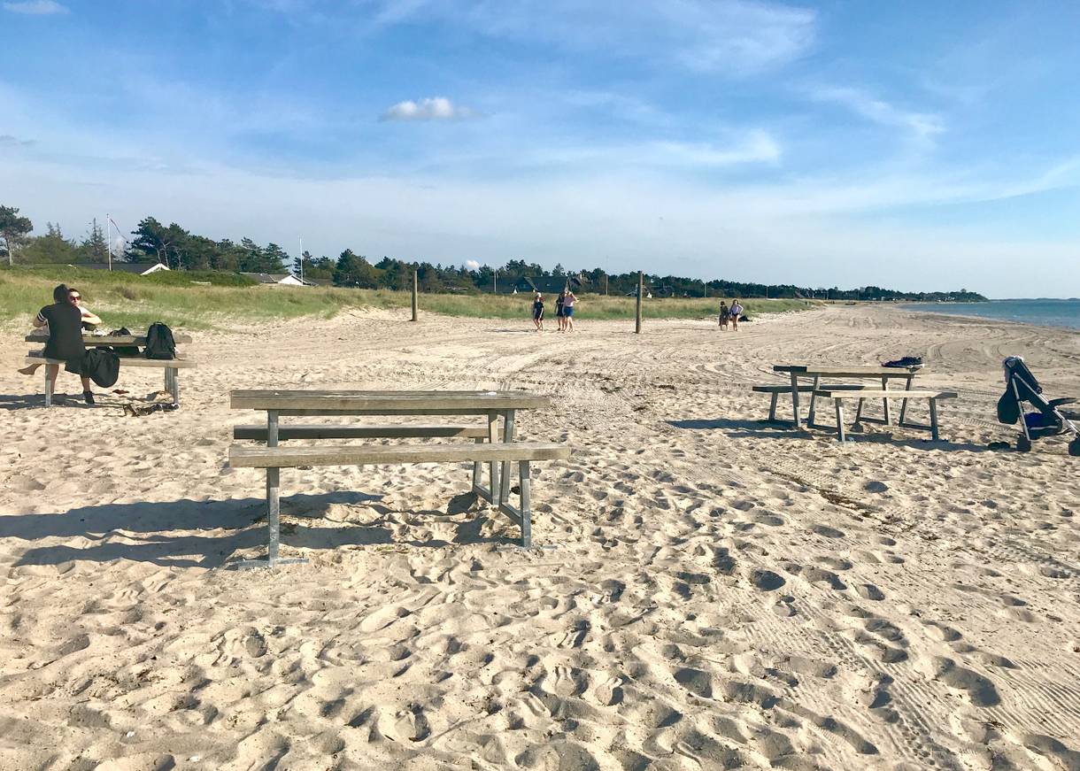 Flacher, sandige Strand mit Strandbesuchern und Picknickbänken