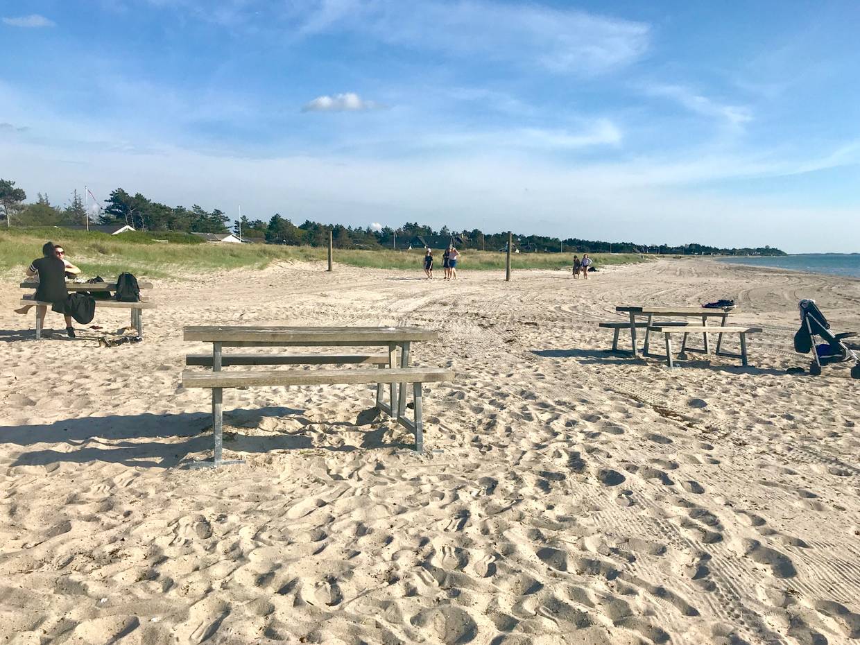 Flacher, sandige Strand mit Strandbesuchern und Picknickbänken