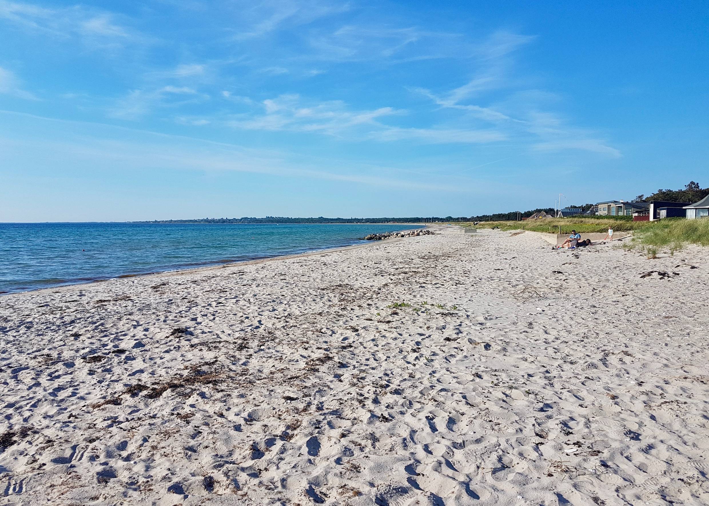 Sandstrand, am Rand einige Ferienhäuser und Badegäste