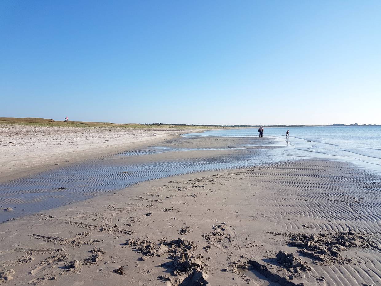 Flacher Sandstrand mit einer Sandbank und Spaziergängern im Hintergrund