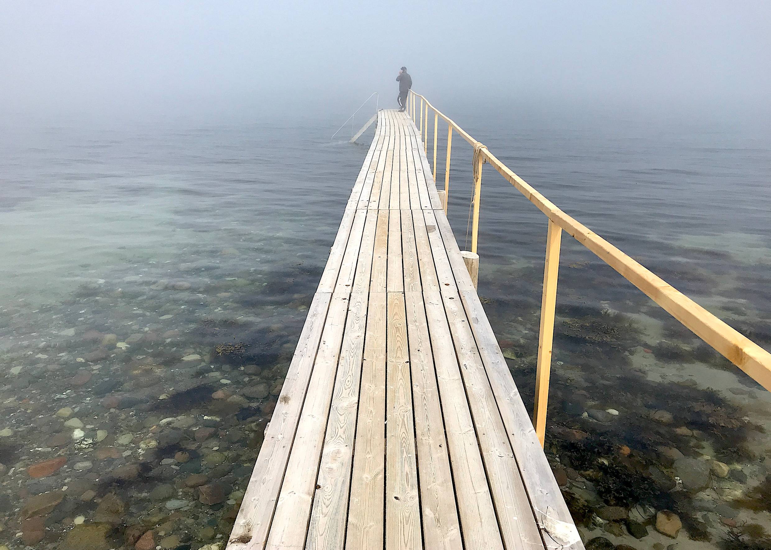Hölzerner Badesteg ins Meer am steinigen Strand